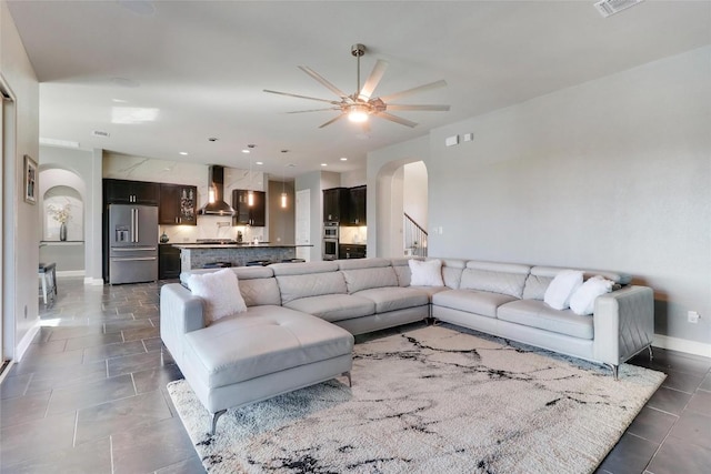 living area featuring dark tile patterned flooring, ceiling fan, arched walkways, and baseboards