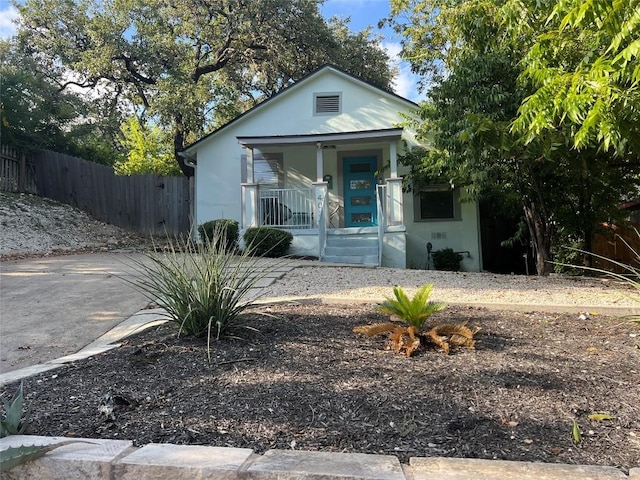 view of front facade with a porch, stucco siding, and fence