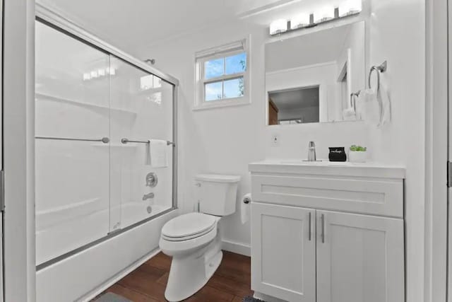 bathroom featuring vanity, toilet, wood finished floors, enclosed tub / shower combo, and baseboards