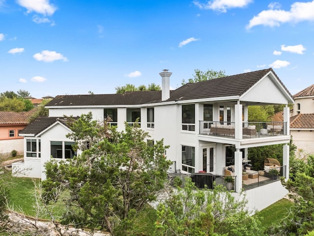 rear view of property with a balcony, stucco siding, french doors, a chimney, and a tiled roof