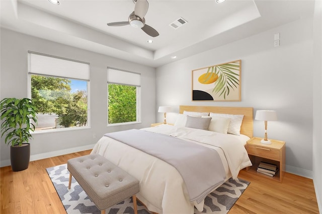 bedroom featuring baseboards, light wood finished floors, and a tray ceiling