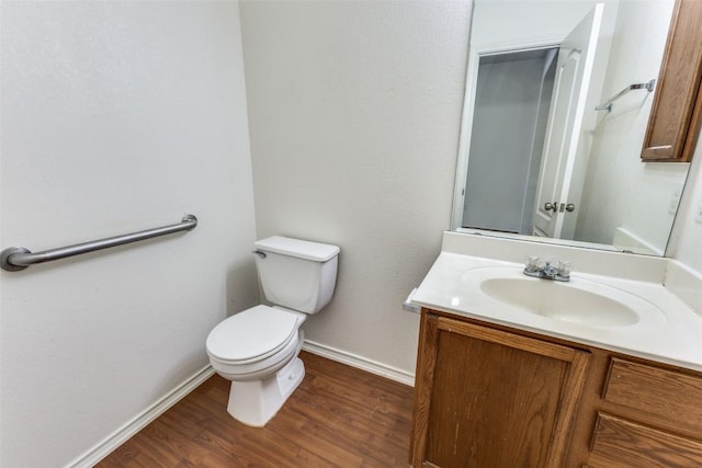 bathroom with toilet, vanity, wood finished floors, and baseboards