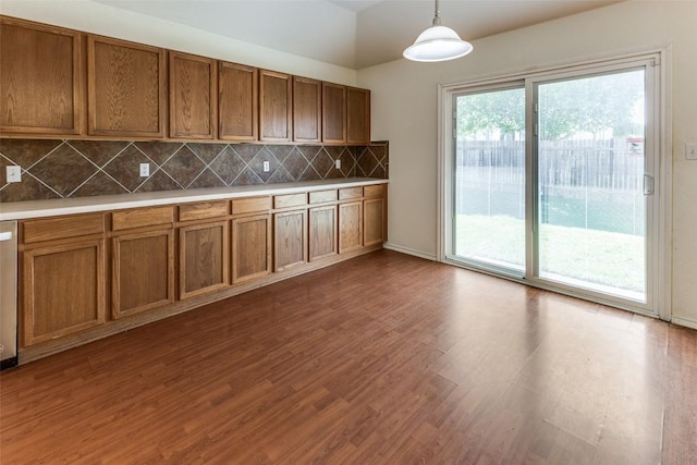 kitchen featuring pendant lighting, tasteful backsplash, vaulted ceiling, brown cabinets, and dark wood-style floors