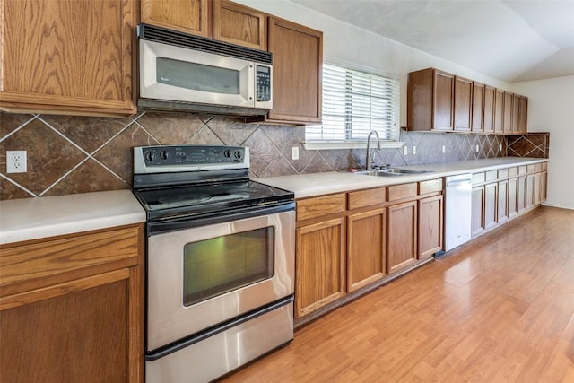 kitchen with a sink, light countertops, appliances with stainless steel finishes, brown cabinetry, and light wood finished floors