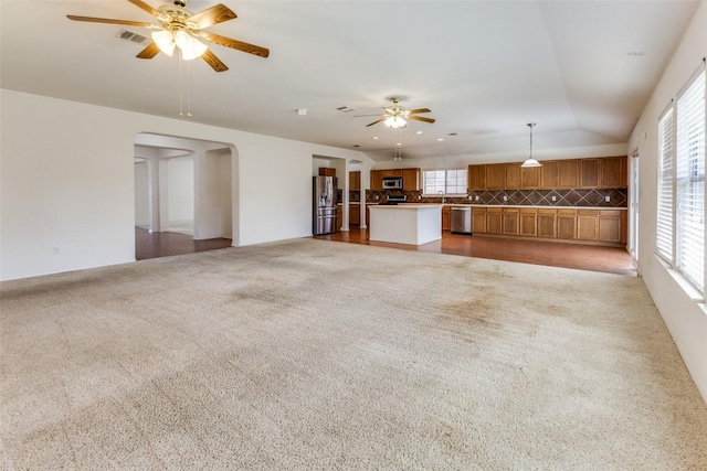 unfurnished living room with vaulted ceiling, visible vents, ceiling fan, arched walkways, and light colored carpet