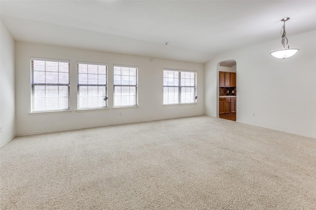 carpeted empty room with arched walkways and baseboards