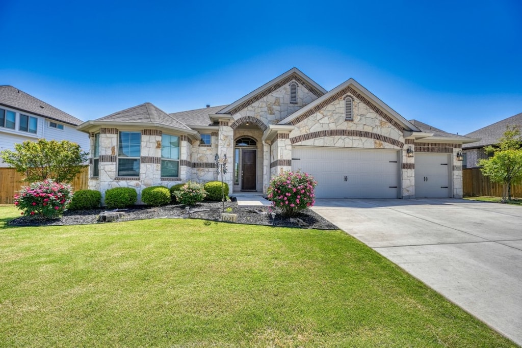 1021 Azul Lagoon Dr, Leander, TX 78641 - french provincial home with driveway, stone siding, an attached garage, a front yard, and fence
