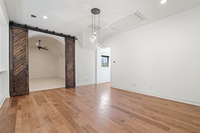 unfurnished living room with attic access, a barn door, recessed lighting, and light wood finished floors