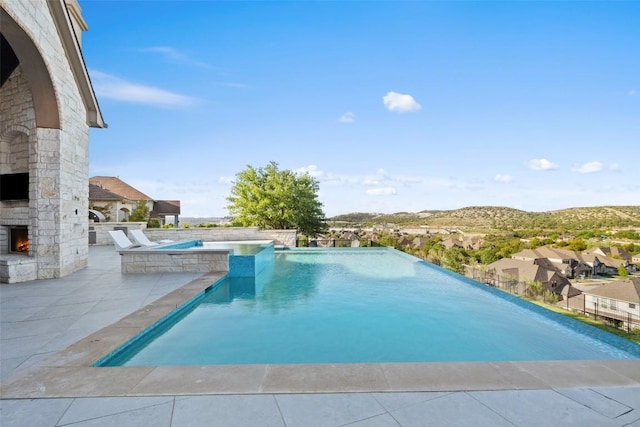 view of swimming pool featuring a patio, an outdoor stone fireplace, and an infinity pool
