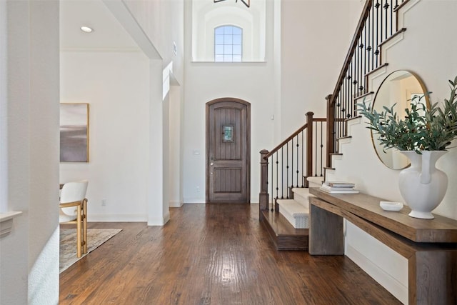 foyer entrance featuring dark wood-style flooring, baseboards, stairway, and a high ceiling