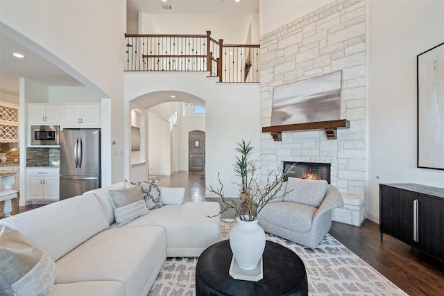 living room with a fireplace, a towering ceiling, wood finished floors, and arched walkways