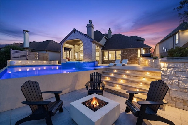 view of swimming pool featuring a fire pit, a patio area, and an infinity pool