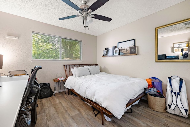 bedroom with a textured ceiling, wood finished floors, ceiling fan, and visible vents