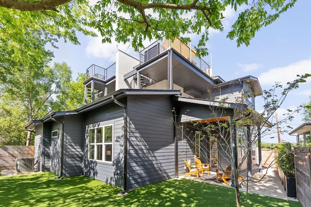 rear view of property with a lawn, fence, and a balcony