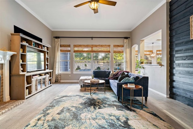 living area with wood finished floors, ceiling fan, plenty of natural light, crown molding, and baseboards