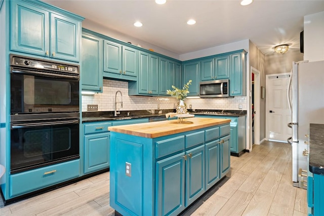 kitchen with wood counters, stainless steel microwave, freestanding refrigerator, blue cabinets, and a sink