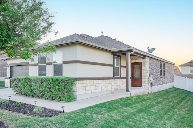view of front of house with fence, stone siding, a garage, stucco siding, and a lawn