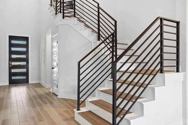 foyer entrance with wood finished floors, arched walkways, baseboards, stairway, and a towering ceiling