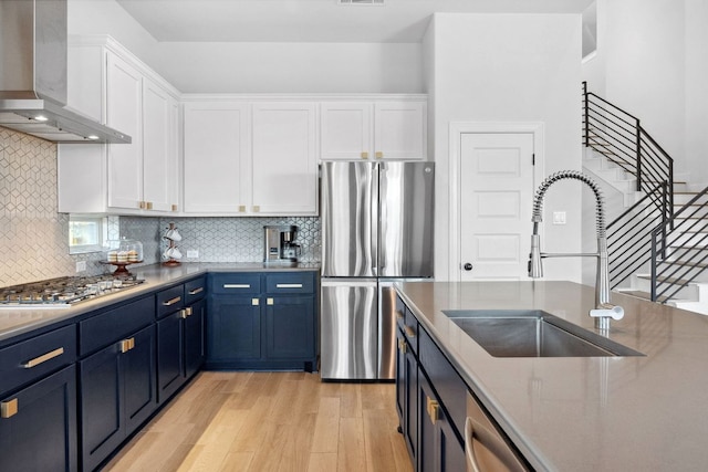 kitchen featuring a sink, appliances with stainless steel finishes, wall chimney exhaust hood, white cabinetry, and blue cabinets