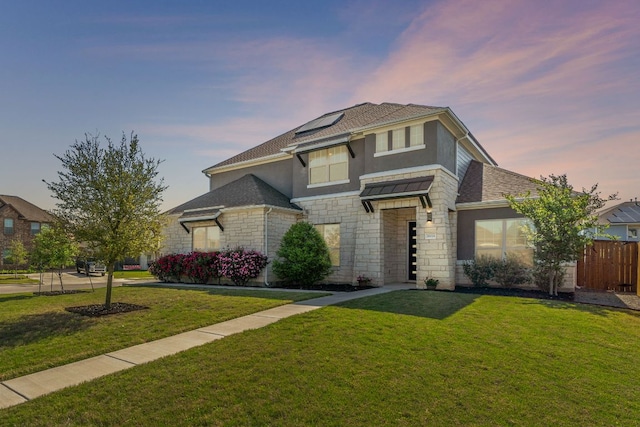 view of front of property with roof mounted solar panels, stone siding, stucco siding, fence, and a front lawn