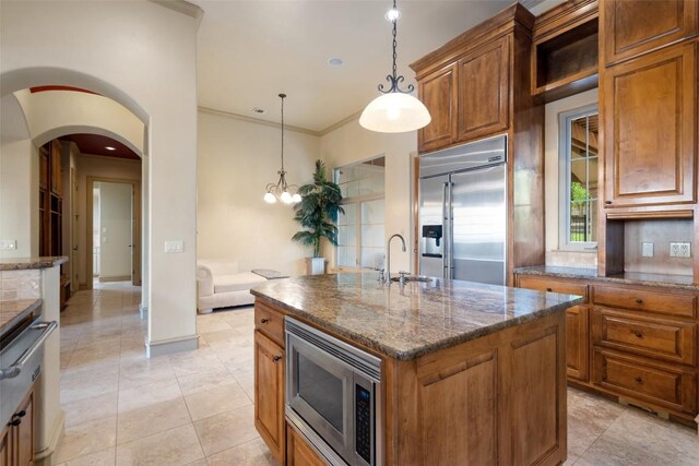 11913 Preserve Vista Ter, Austin, TX 78738 - kitchen with built in appliances, brown cabinets, dark stone counters, decorative light fixtures, and an island with sink