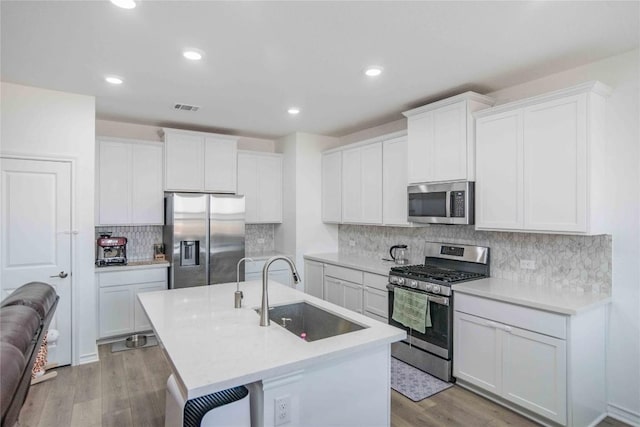kitchen featuring recessed lighting, an island with sink, a sink, decorative backsplash, and appliances with stainless steel finishes