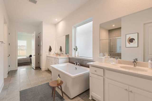 300 Alava Way, Georgetown, TX 78628 - ensuite bathroom featuring two vanities, a soaking tub, a shower stall, tile patterned floors, and recessed lighting