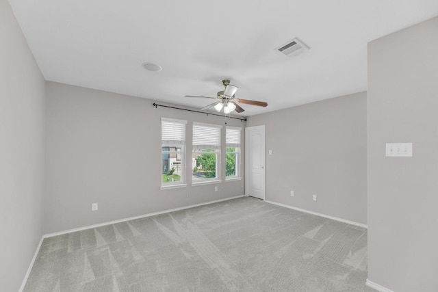 spare room featuring light colored carpet, visible vents, baseboards, and a ceiling fan