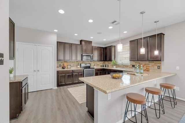 kitchen with dark brown cabinetry, a peninsula, a breakfast bar, appliances with stainless steel finishes, and light wood finished floors