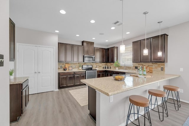 1114 Sussex Pl, Round Rock, TX 78665 - kitchen featuring stainless steel appliances, light wood-style flooring, dark brown cabinets, a peninsula, and a kitchen bar
