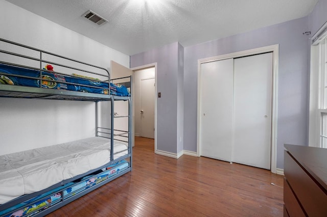 unfurnished bedroom with a closet, a textured ceiling, baseboards, visible vents, and wood finished floors