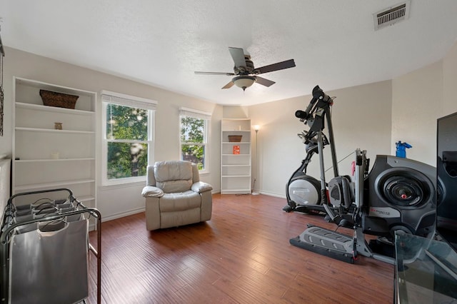exercise area featuring a ceiling fan, baseboards, visible vents, and wood finished floors