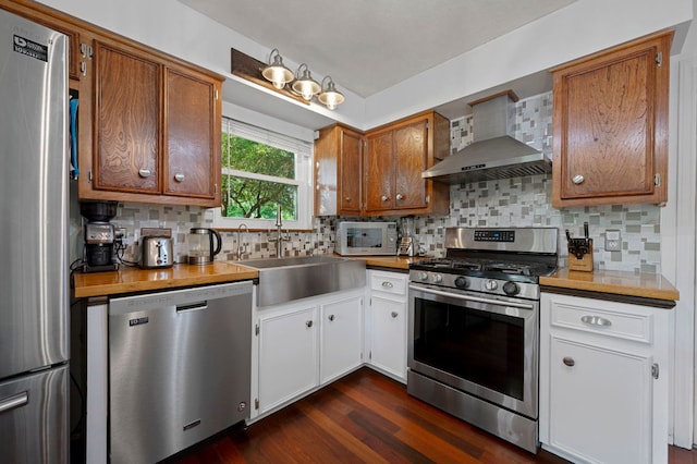 kitchen featuring dark wood finished floors, a sink, wall chimney range hood, stainless steel appliances, and tasteful backsplash