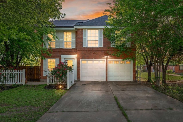 traditional home featuring driveway, brick siding, fence, an attached garage, and roof mounted solar panels