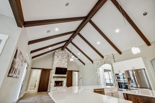 1609 Havenwood Blvd, New Braunfels, TX 78132 - kitchen featuring a sink, beamed ceiling, a ceiling fan, a stone fireplace, and a large island with sink