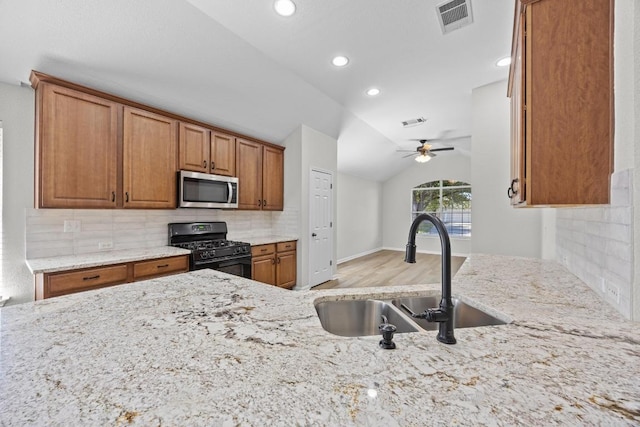 806 Broken Trace Ct, Round Rock, TX 78665 - kitchen featuring black gas range oven, stainless steel microwave, a sink, light stone countertops, and lofted ceiling