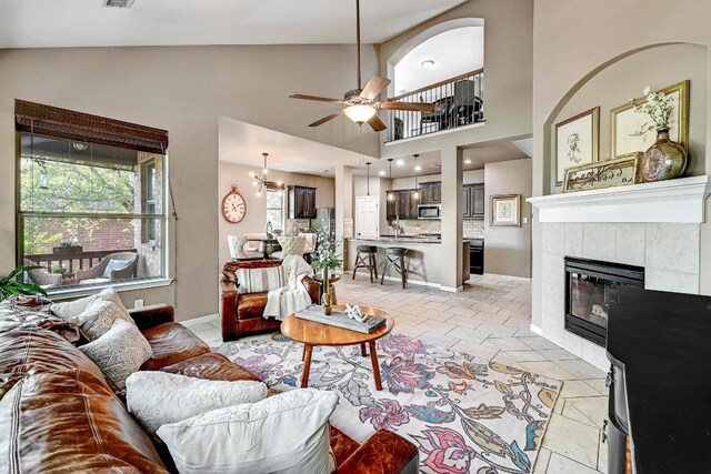 21940 Agarito Ln, Spicewood, TX 78669 - living room with ceiling fan, light tile patterned floors, a tiled fireplace, high vaulted ceiling, and baseboards