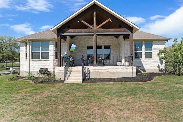 rear view of house featuring stone siding, a yard, and covered porch