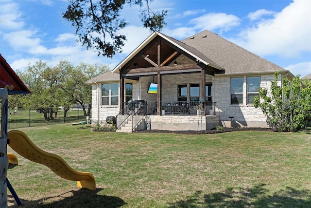 back of house featuring stone siding, a playground, covered porch, and roof with shingles