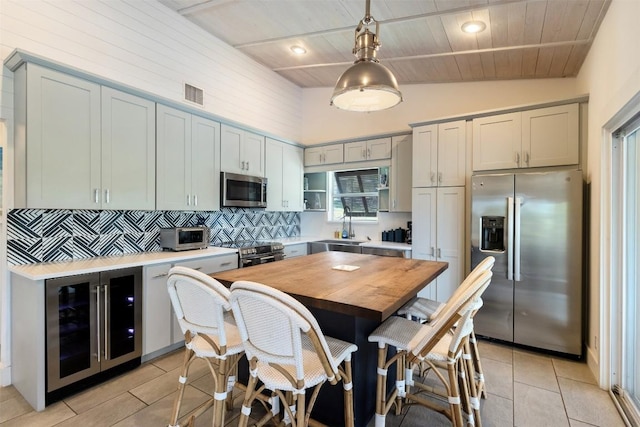 kitchen with appliances with stainless steel finishes, beverage cooler, a sink, tasteful backsplash, and decorative light fixtures