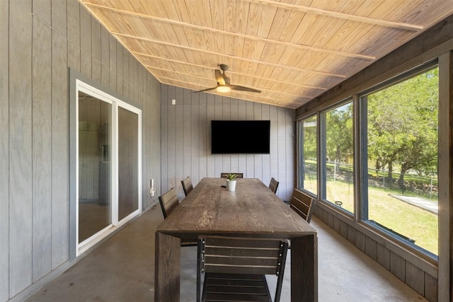 sunroom with concrete flooring, ceiling fan, wooden walls, lofted ceiling, and outdoor dining space