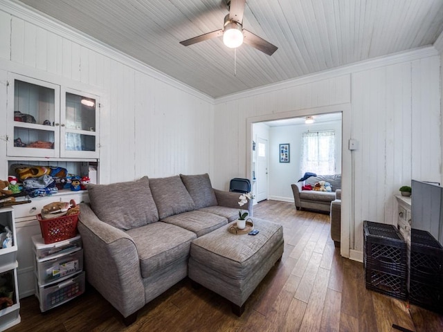 living area featuring a ceiling fan, dark wood-type flooring, wooden walls, and ornamental molding