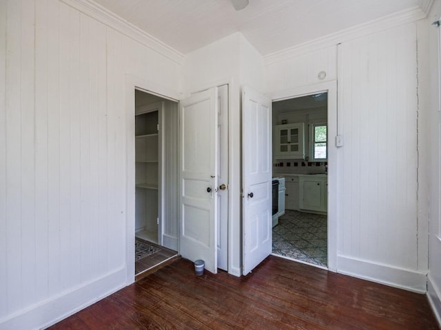 unfurnished bedroom featuring ensuite bathroom, baseboards, ornamental molding, wooden walls, and dark wood-type flooring