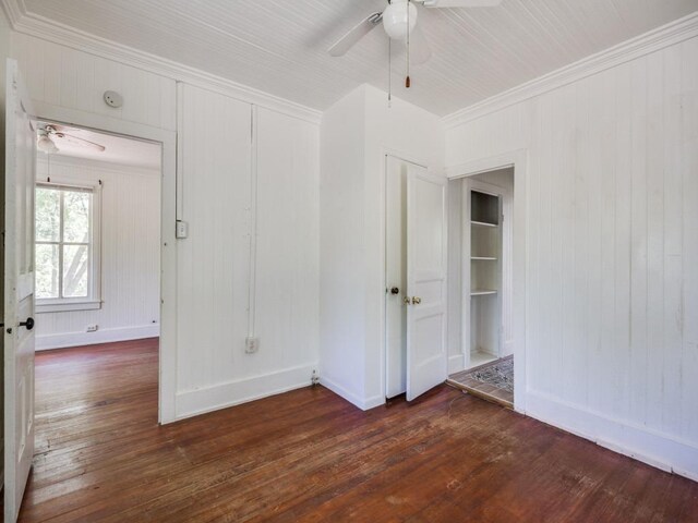 unfurnished room featuring baseboards, wooden walls, crown molding, dark wood-type flooring, and ceiling fan