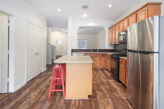 2025 Wayward Sun Dr, Austin, TX 78754 - kitchen featuring black appliances, a kitchen island, dark wood-style floors, a breakfast bar area, and arched walkways
