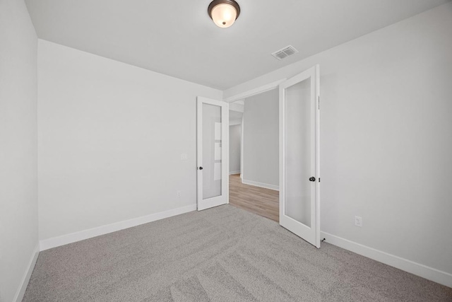 carpeted spare room with visible vents, baseboards, and french doors