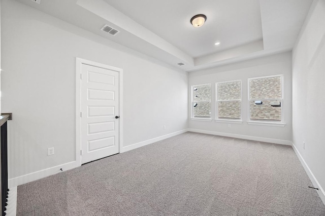 carpeted spare room with visible vents, baseboards, and a raised ceiling