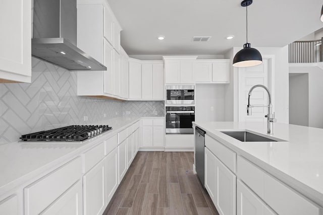 kitchen with wall chimney range hood, light countertops, visible vents, appliances with stainless steel finishes, and a sink