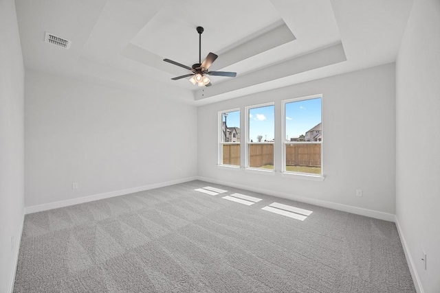 empty room featuring carpet floors, baseboards, a raised ceiling, and visible vents