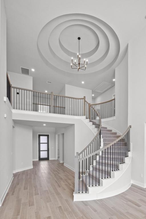 stairway featuring visible vents, a raised ceiling, a high ceiling, and wood finished floors